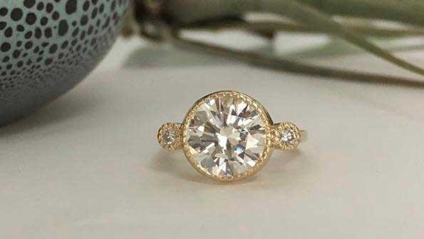 14k yellow gold custom engagement ring with round white diamond center stone and two pave diamonds with milgrain detail