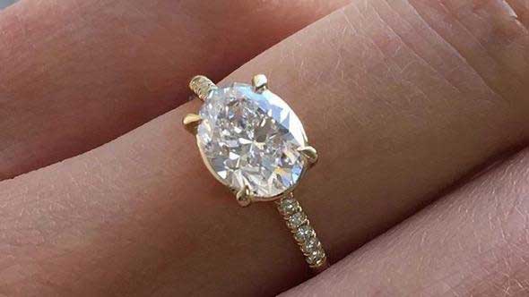 14k yellow gold custom engagement ring with oval cut white diamond center stone and pave equilibrium white diamonds on hand