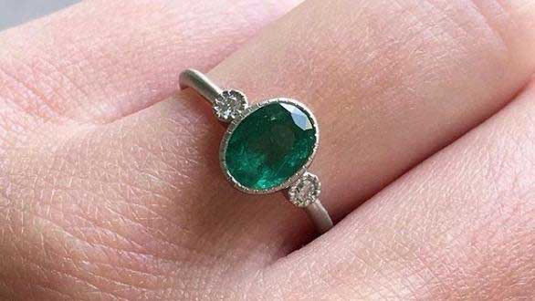 14k yellow gold custom ring with oval emerald with two white side diamonds and milgrain detail