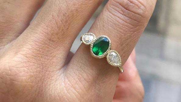 14k yellow gold custom ring with oval cut emerald with milgrain detail and two pear cut white diamonds on hand