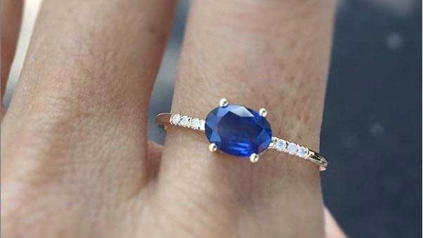 14k yellow gold custom ring with oval cut blue sapphire and white diamond pave equilibrium stones on hand 