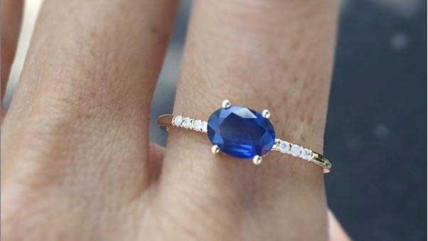 14k yellow gold custom ring with oval cut blue sapphire and white diamond pave equilibrium stones on hand