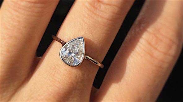14k yellow gold custom ring with pear shaped white diamond center stone on hand