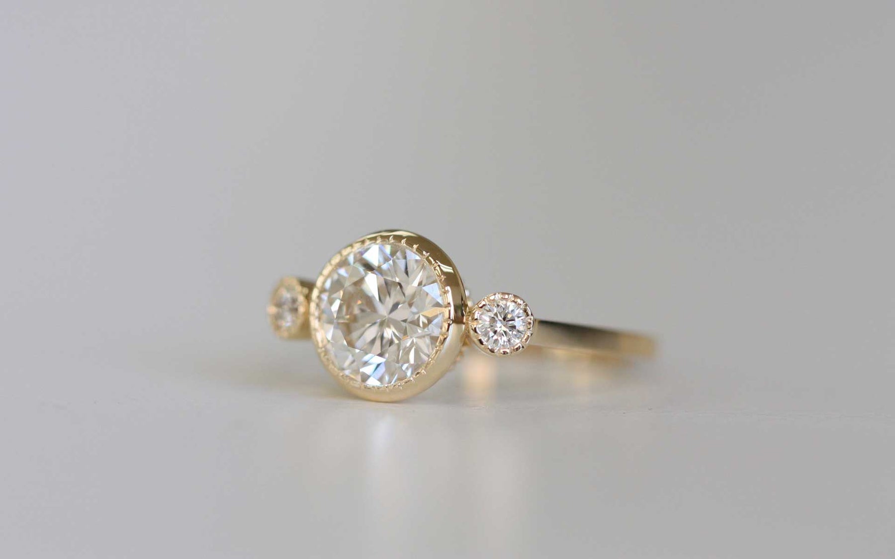 14k yellow gold custom engagement ring with white diamond round cut center stone and two white diamond side stones with milgrain detail
