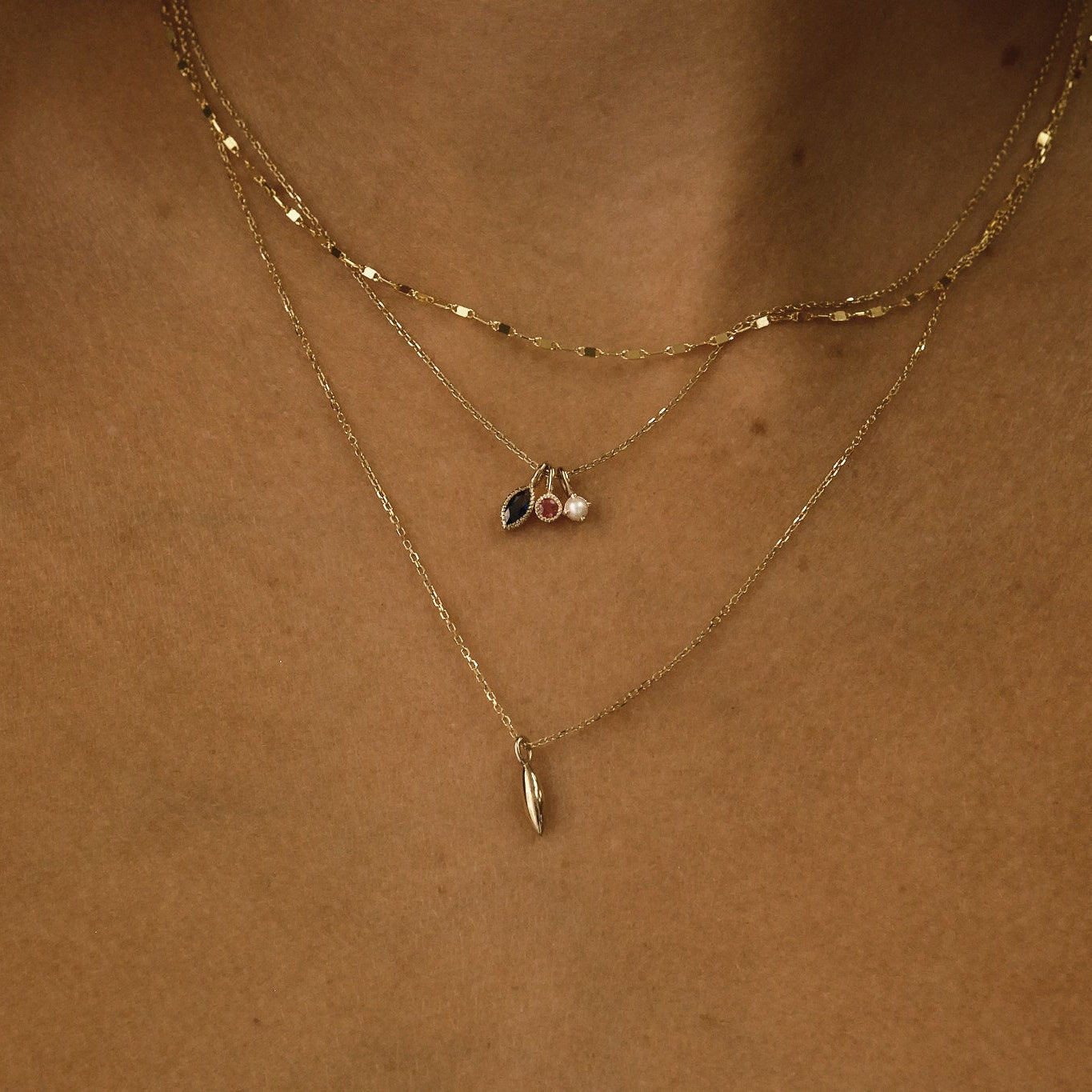 Close-up of a person wearing two gold necklaces with pendants on a neutral background