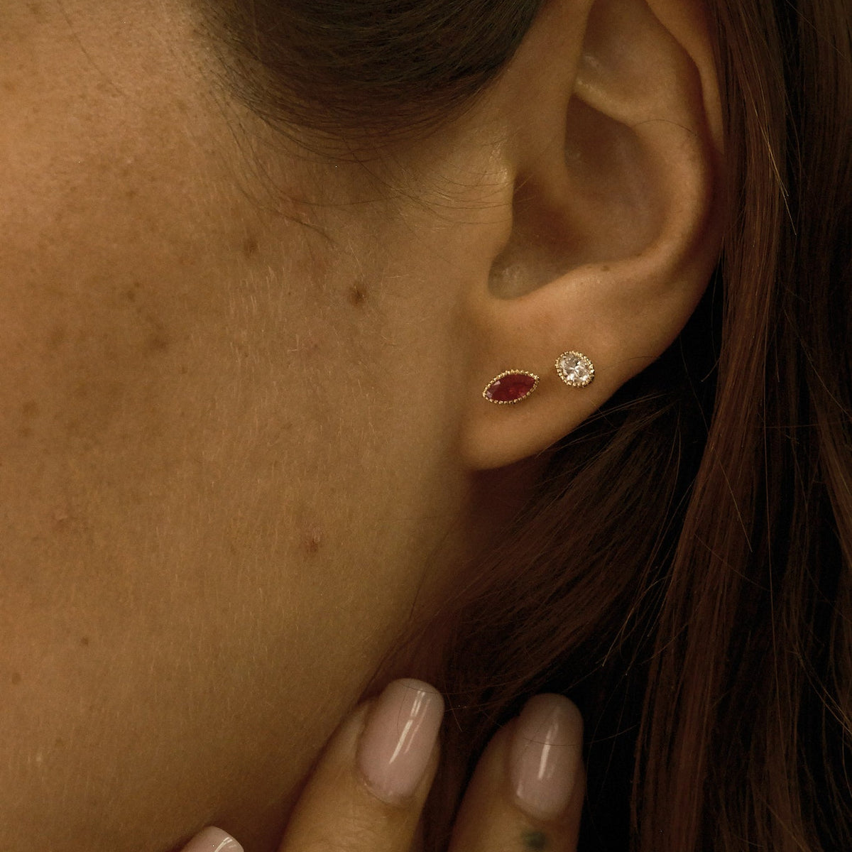 Close-up of an ear wearing two earrings with a hand touching the side of the face.