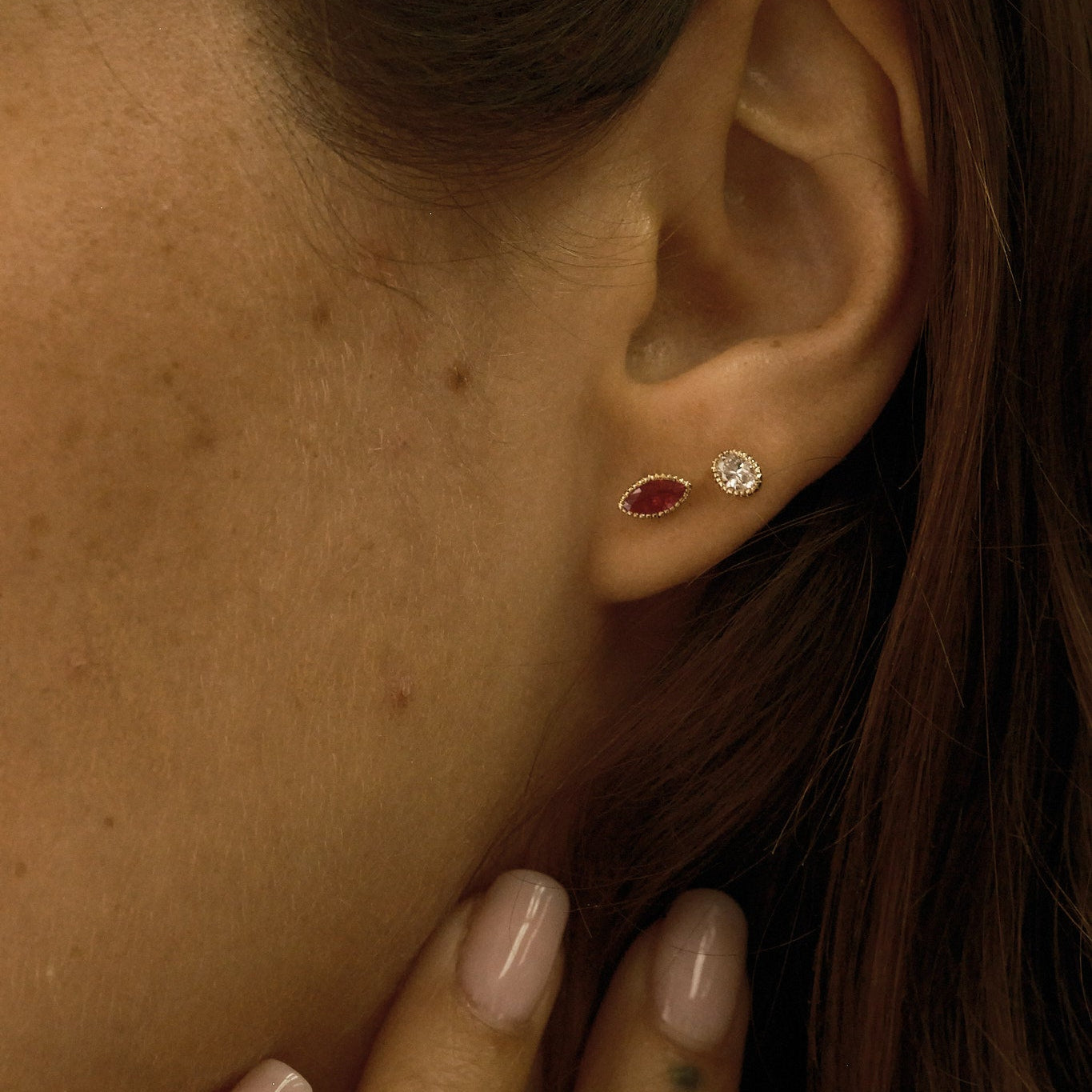 Close-up of an ear wearing two earrings with a hand touching the side of the face.