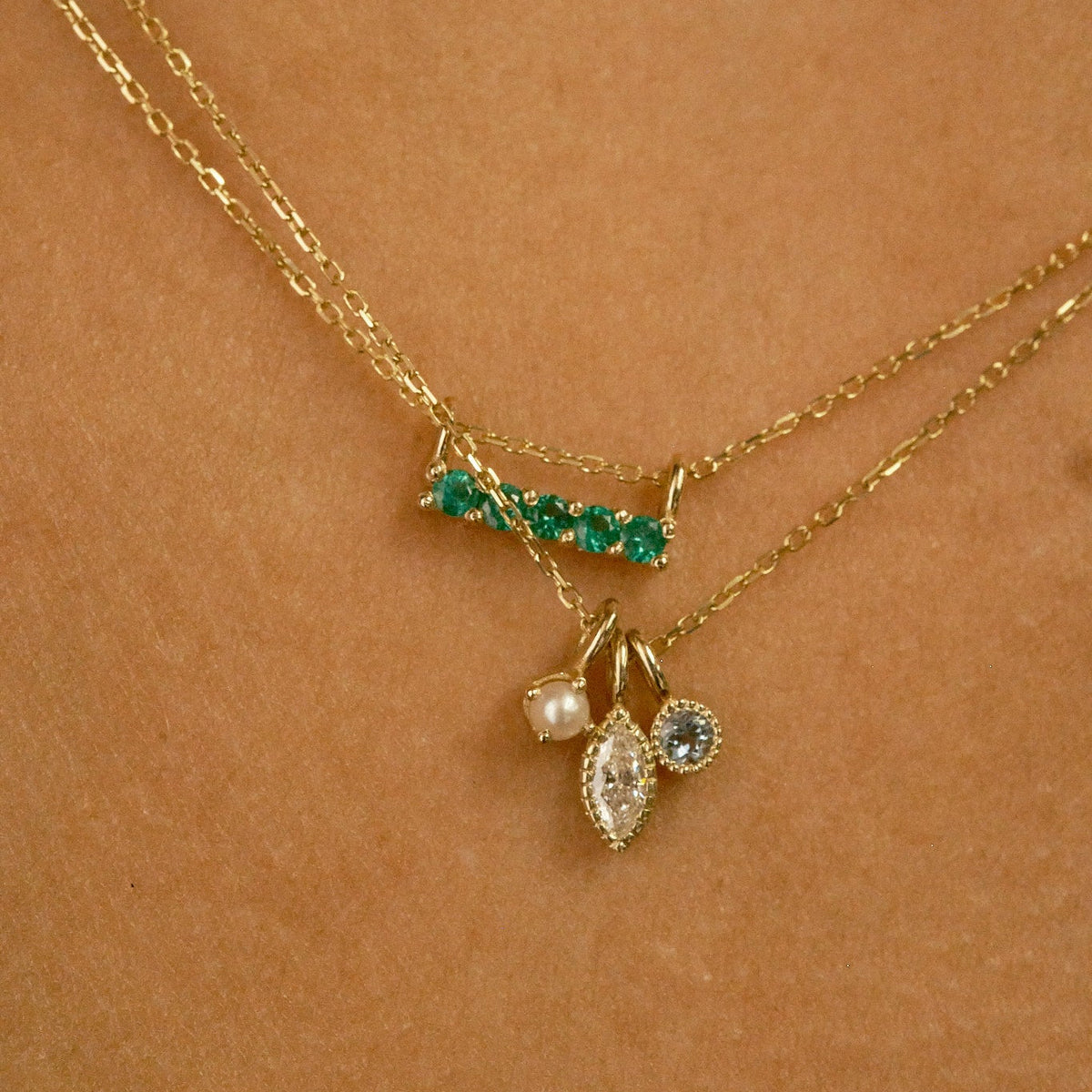 Gold necklace with green gemstones and three pendant drops on a brown background