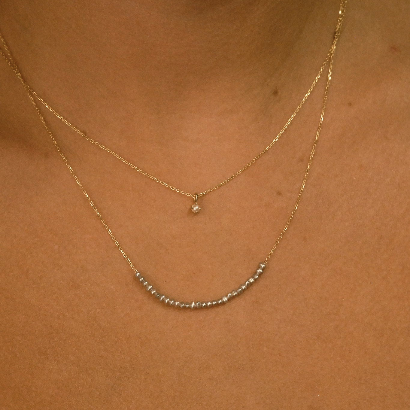 Close-up of a person wearing two gold necklaces on a plain background