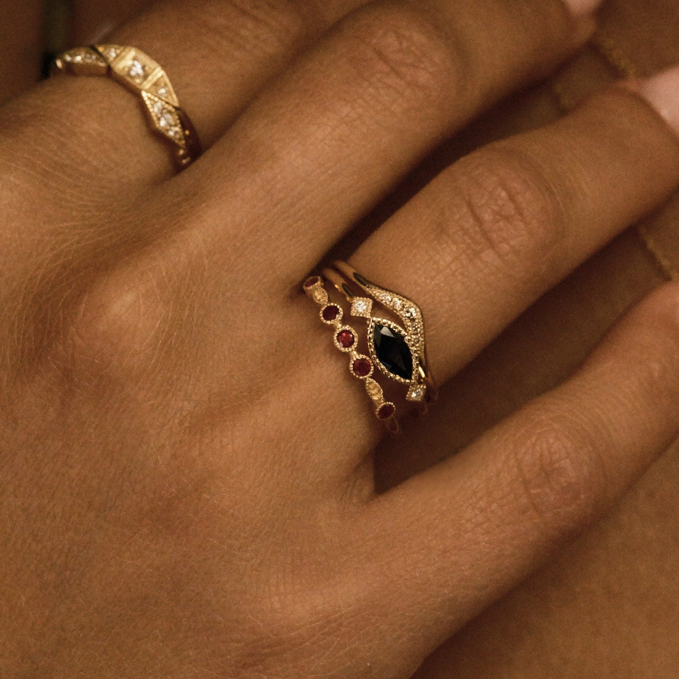 Close-up of a hand wearing two gold rings with gemstones on a brown background