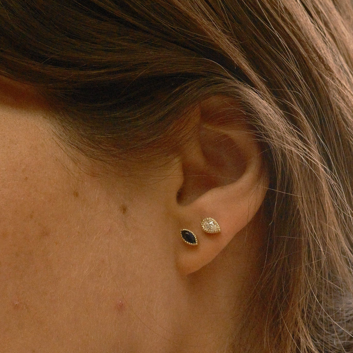 Close-up of a person wearing two earrings: one black and one clear.