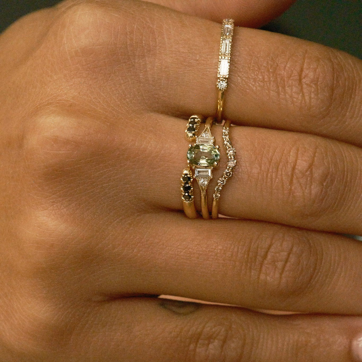 Close-up of a hand wearing multiple rings with gemstones and gold bands.