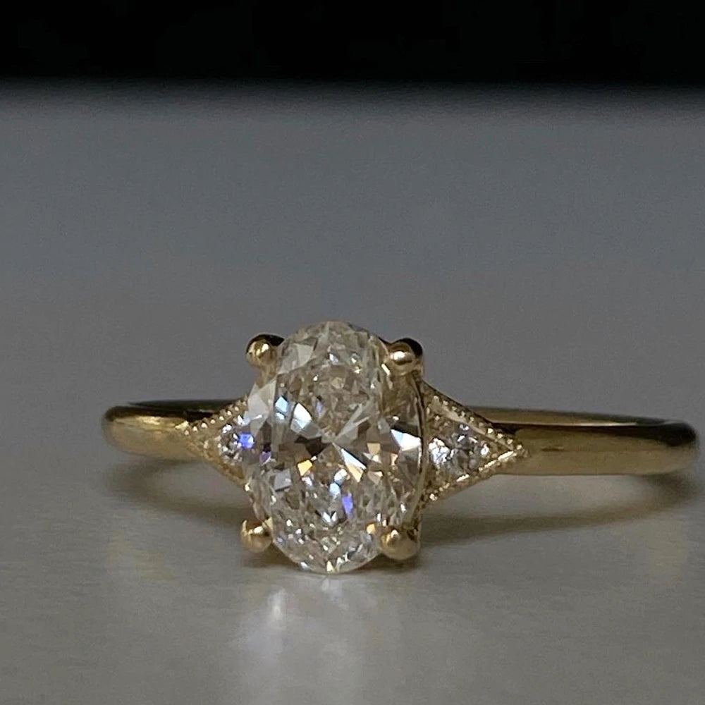 14k yellow gold custom engagement ring with oval cut white diamond center stone and white diamond side stones and milgrain detail