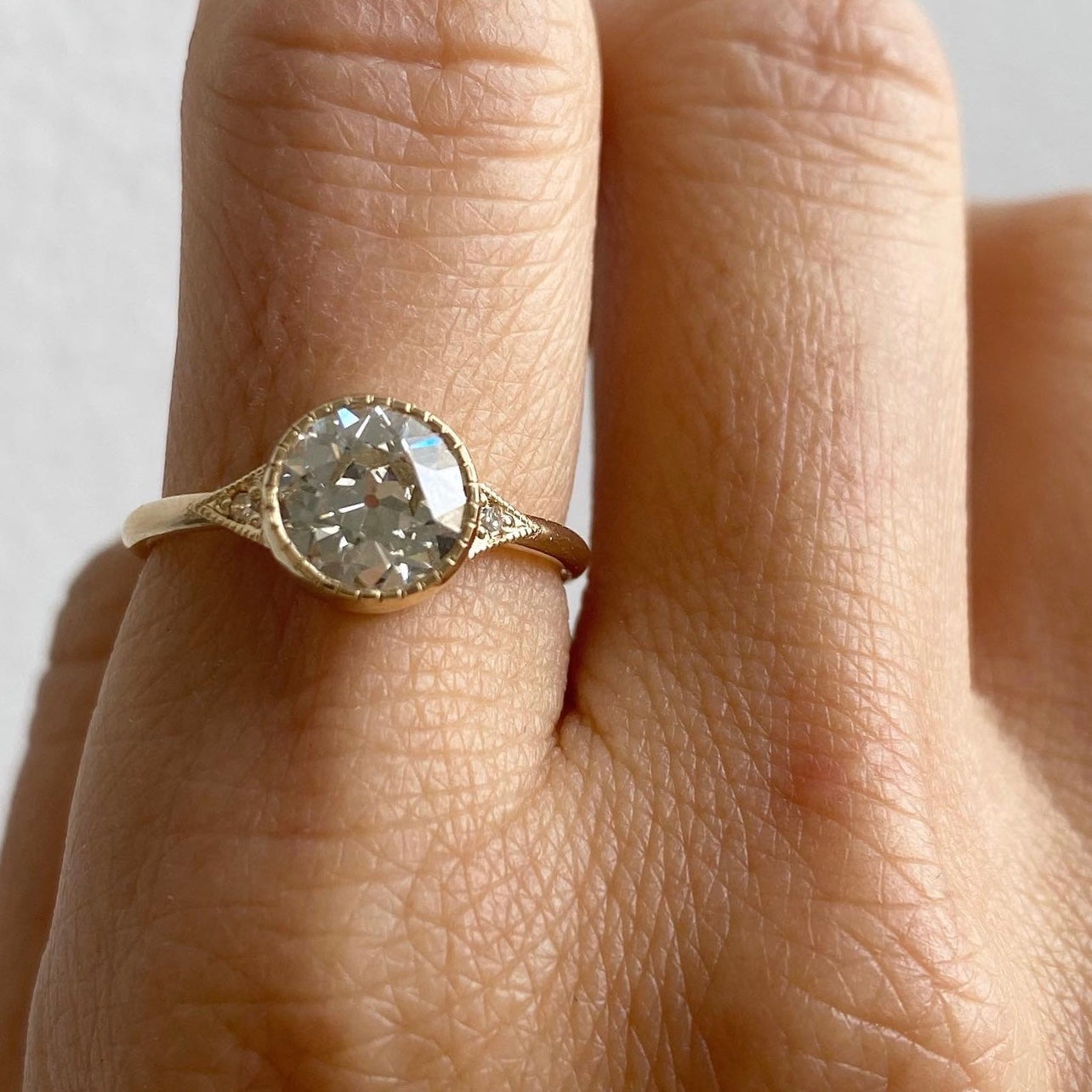 14k yellow gold custom ring with round cut white diamond center stone with milgrain detail and white side diamonds 