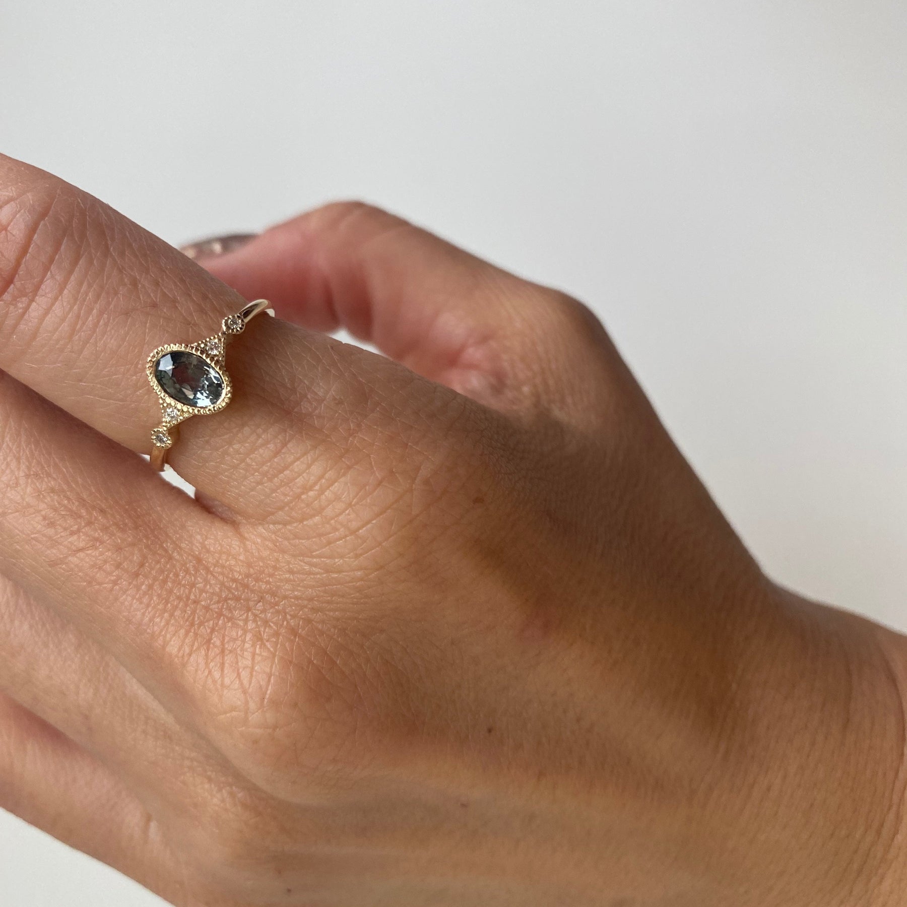 14k yellow gold custom ring with oval cut white diamond center stone and pave white diamond side stones on hand