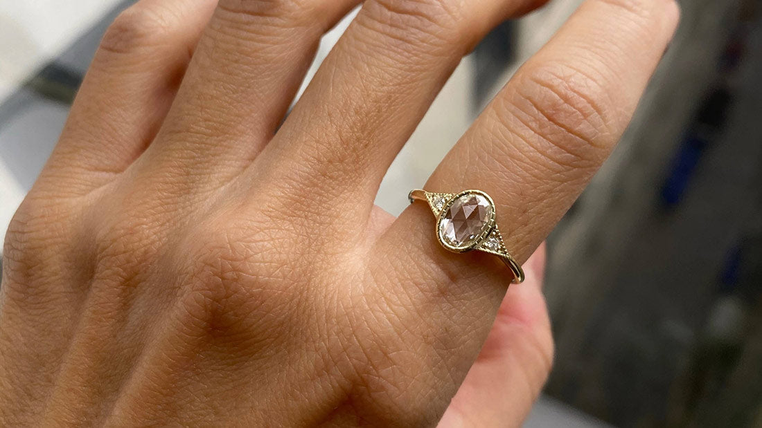 14k yellow gold custom engagement ring with oval white diamond center stone and pave diamonds on hand
