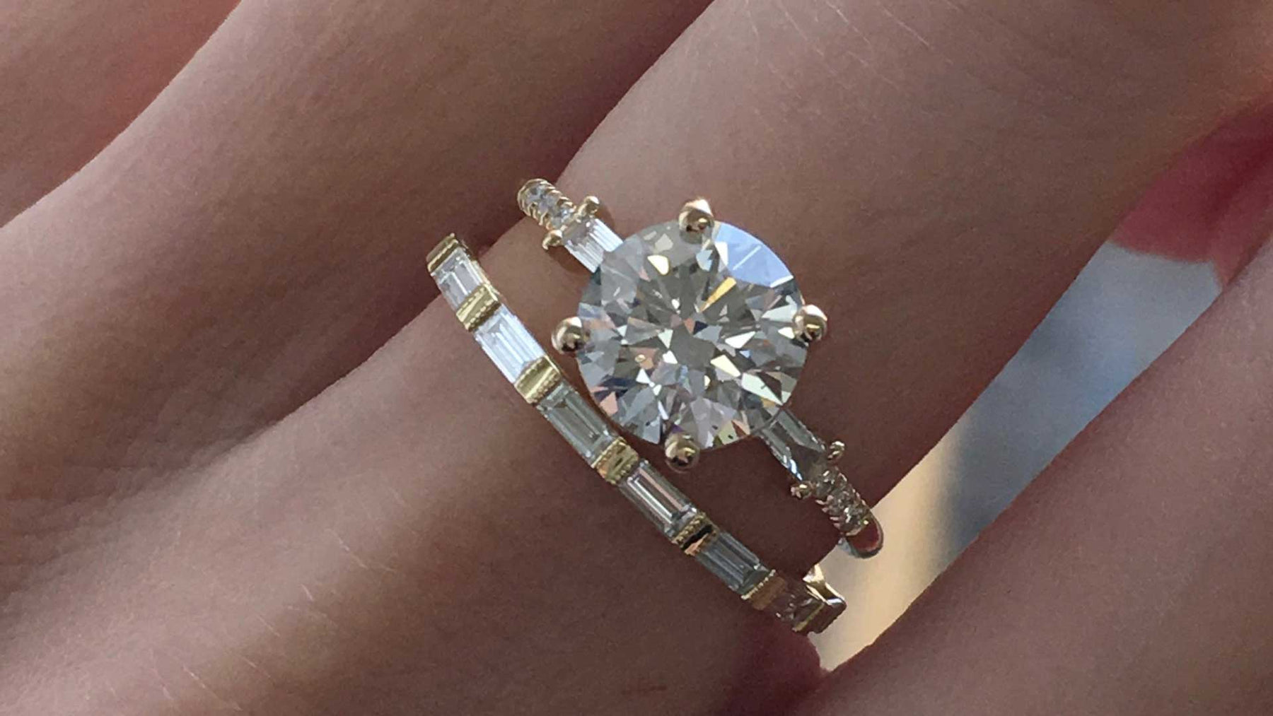 14k yellow gold custom engagement ring with brilliant cut white diamond center stone and baguette white diamonds stacked with baguette white diamond wedding band on hand