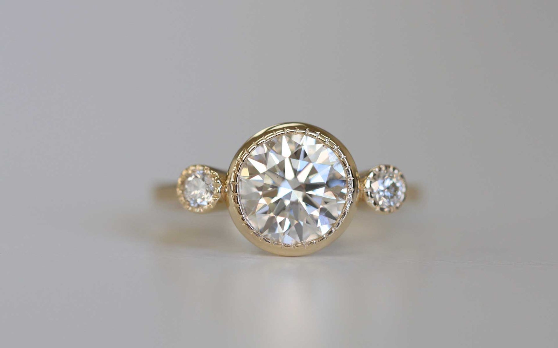 14k yellow gold custom engagement ring with round cut white diamond center stone and two white diamonds with milgrain detail