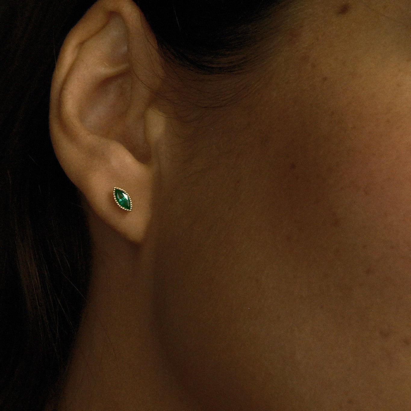 Close-up of an ear with a green gemstone earring.
