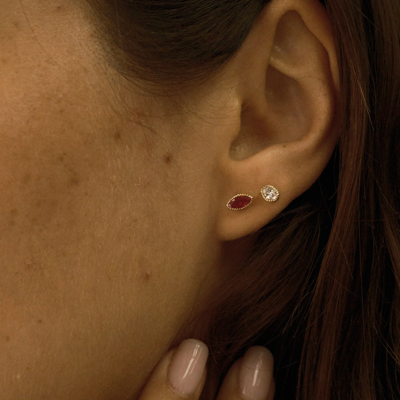 Close-up of an ear wearing two earrings with a hand touching the side of the face.