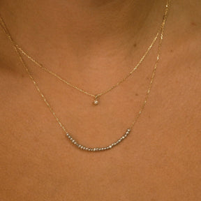 Close-up of a person wearing two gold necklaces on a plain background