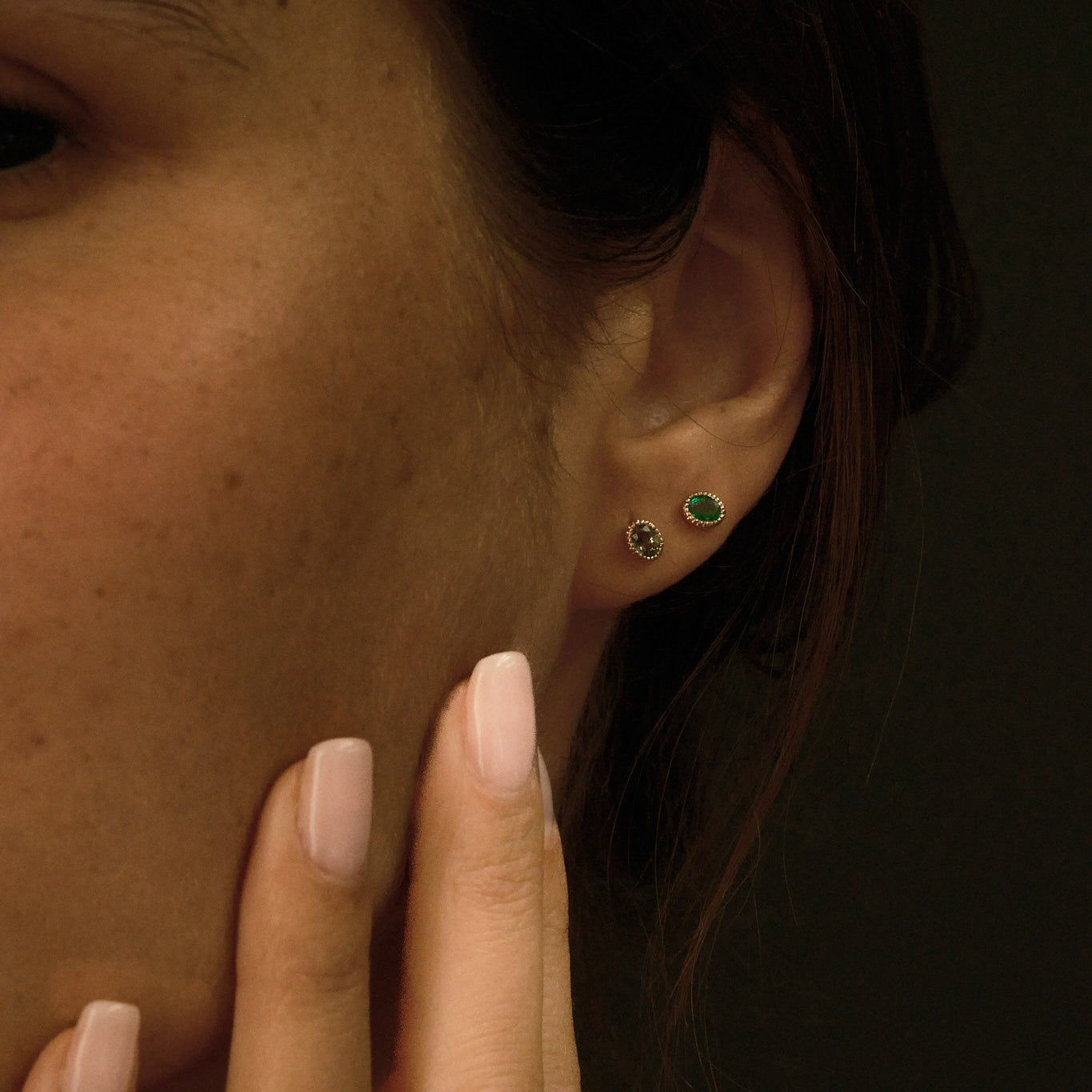 Close-up of a person wearing gold earrings and a gold ring with a dark background