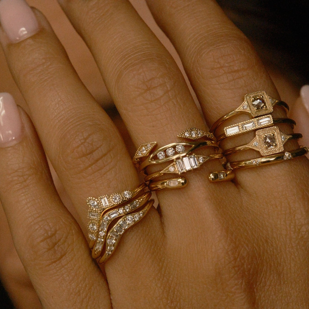 Close-up of a hand wearing multiple gold rings with diamond accents on a dark background