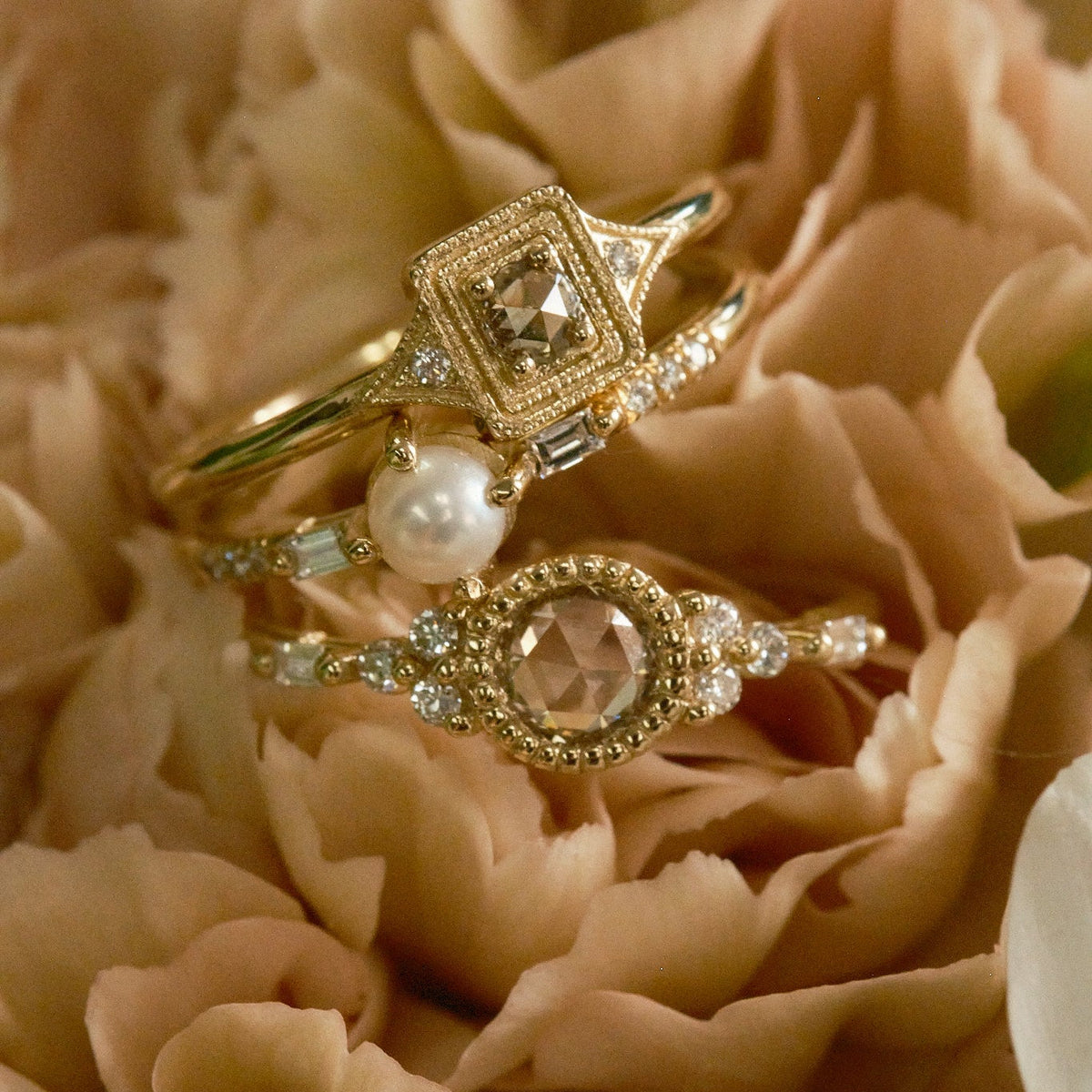 Three gold rings with gemstones and pearls on a floral background