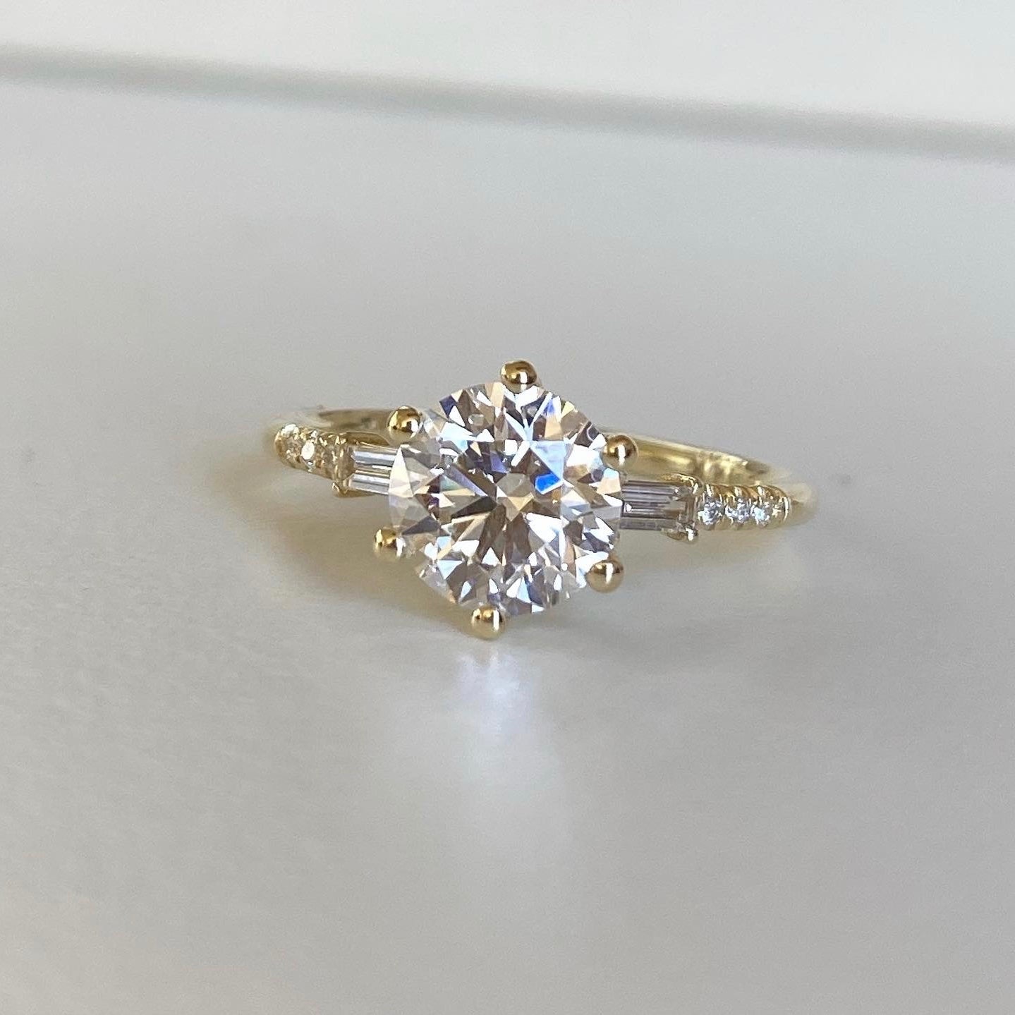 14k yellow gold custom engagement ring with round cut white diamond center stone and white diamond baguette and pave white diamonds
